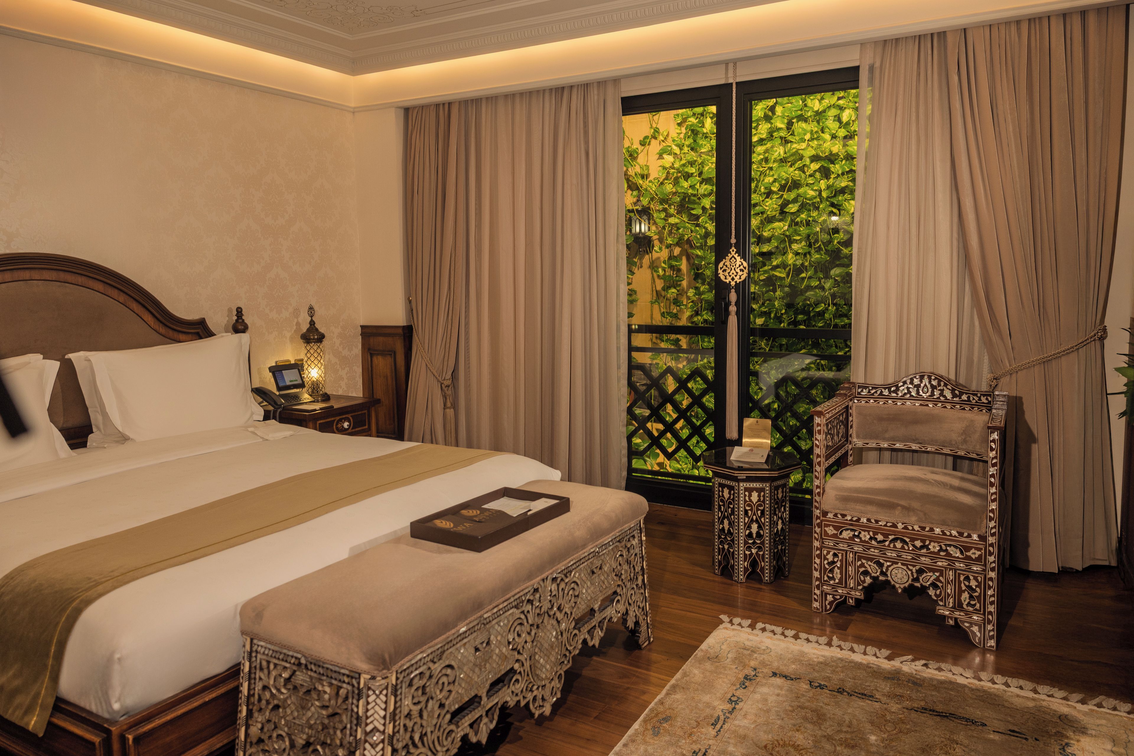 Habitación de hotel con una cama grande, una silla, una mesita y vistas a zonas verdes por la ventana.