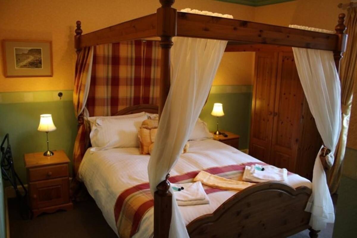 A four-poster bed with a canopy, two bedside tables with lamps, and a green wall with a framed picture.