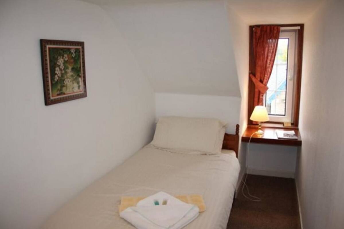A small, single-bed room with a bedside table, a lamp, and a framed picture on the wall.