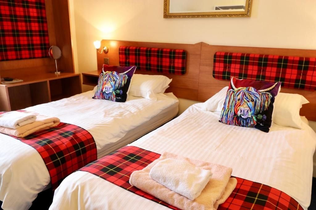 A hotel room with two beds, each with a red plaid bedspread and matching pillows.