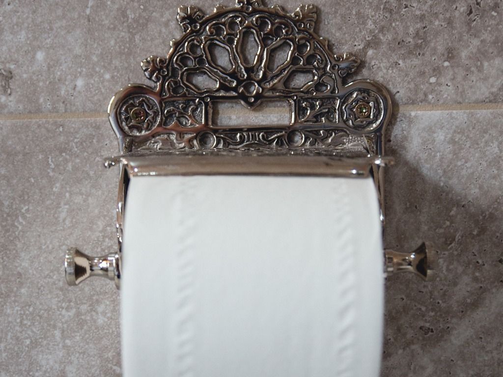 A toilet paper holder with an ornate metal design on a tiled wall.
