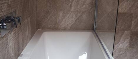 Une salle de bain moderne dotée d’une grande baignoire, d’un espace douche et d’un porte-serviettes fixé au mur.
