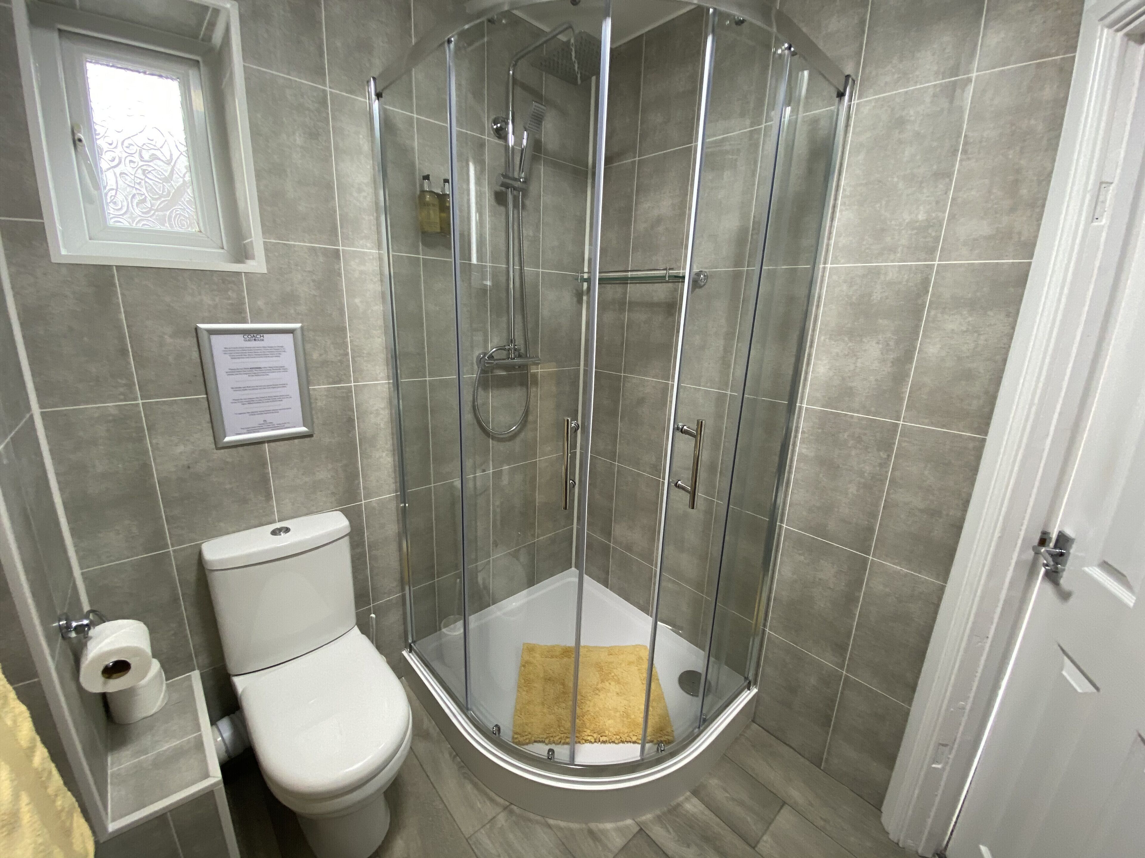 Un bagno angolare con doccia vetro-murata, un water e un cartello illustrativo incorniciato a parete.