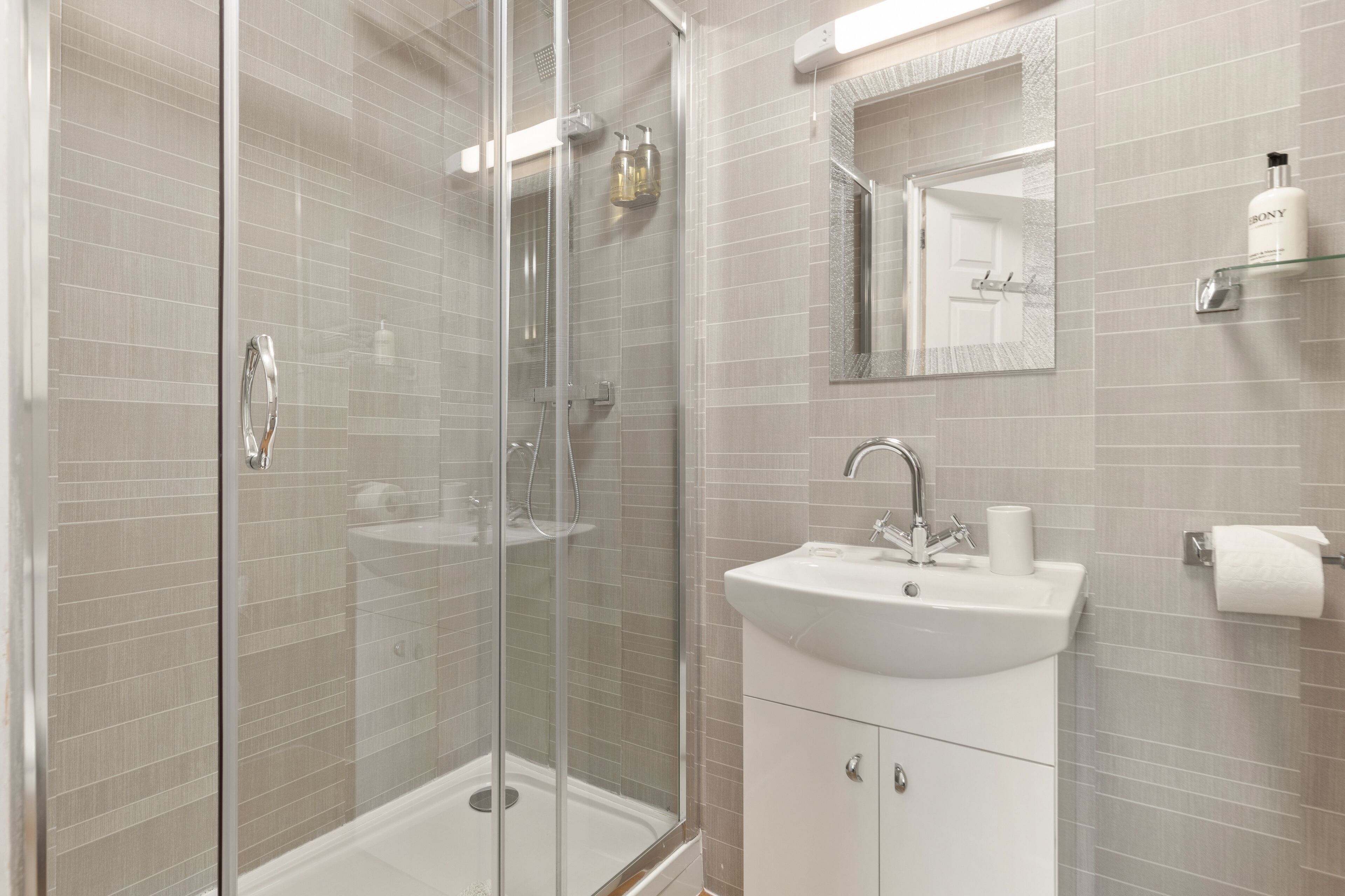 A modern bathroom with a glass-enclosed shower, a white sink, and a mirror above it.