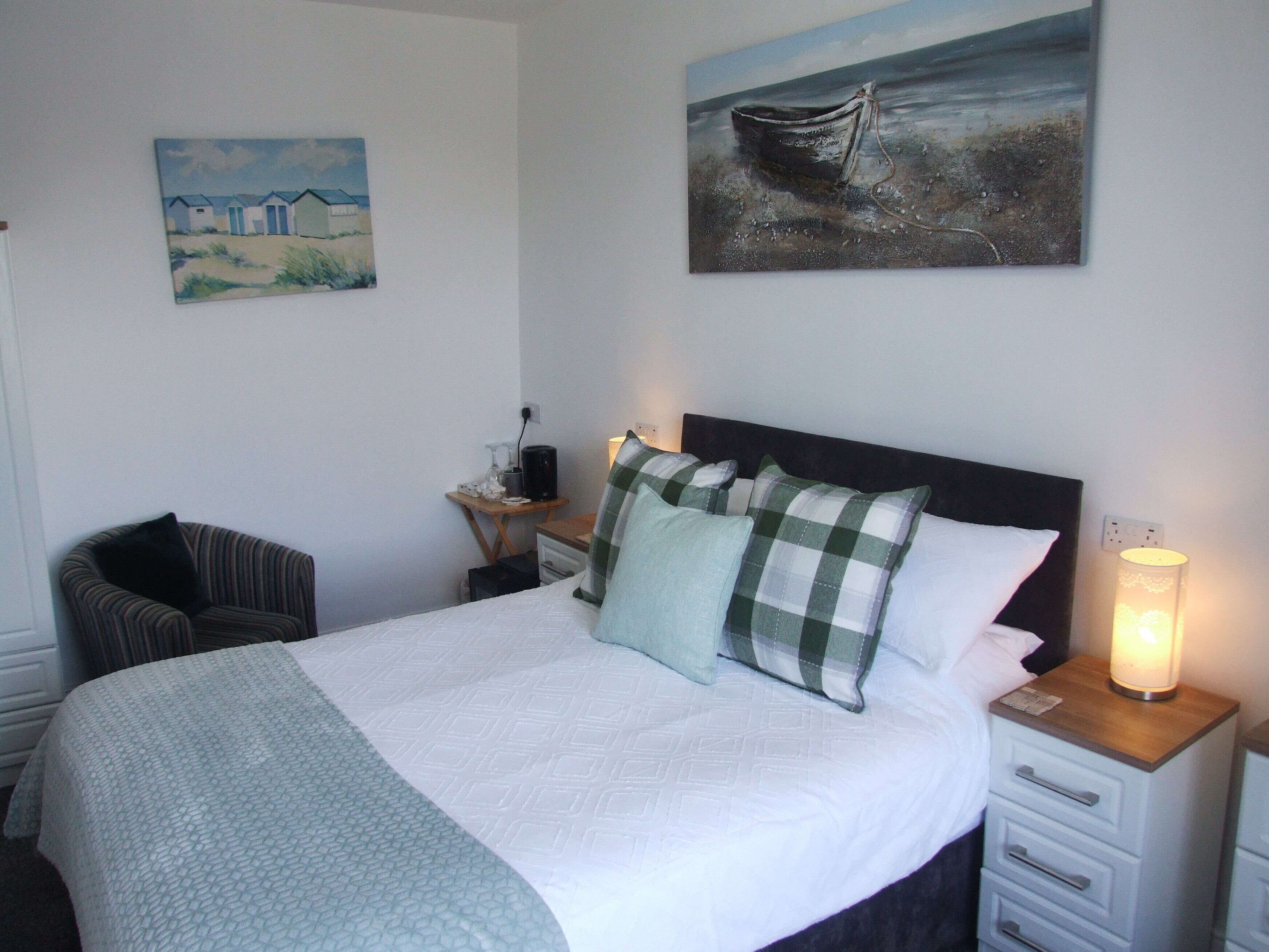 A neatly arranged bedroom with a bed, a chair, a bedside table, and a lamp.