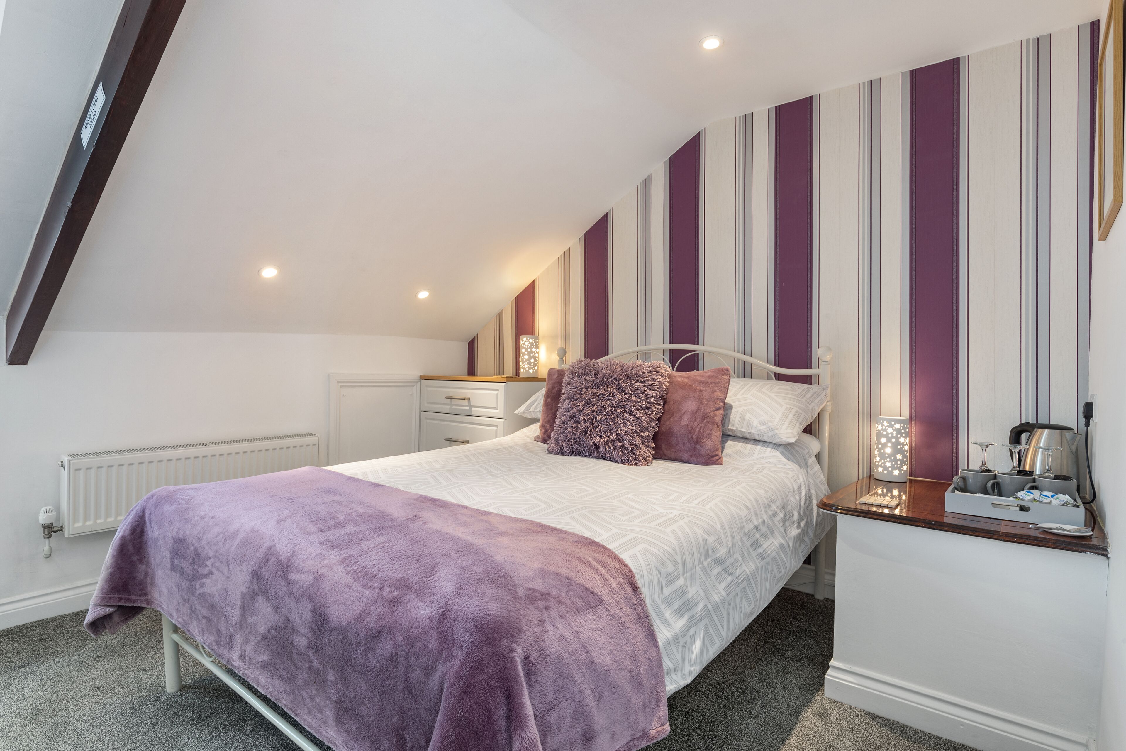 A bedroom with a bed, a nightstand, a lamp, and a radiator.