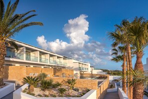 A modern hotel with a pool area, palm trees, and a clear blue sky.