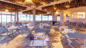 Un vaste espace dédié à la salle à manger, doté de hauts plafonds et baigné de lumière naturelle grâce à de grandes fenêtres. Les tables sont disposées avec soin, accompagnées de chaises, et le plafond présente un motif tissé original.