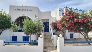 Un bâtiment blanc avec une enseigne indiquant « hôtel Évian ». Il est doté d’une porte bleue, d’un escalier en pierre et de plantes à fleurs roses.