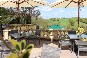 An outdoor patio with wicker furniture and umbrellas, overlooking a green landscape.
