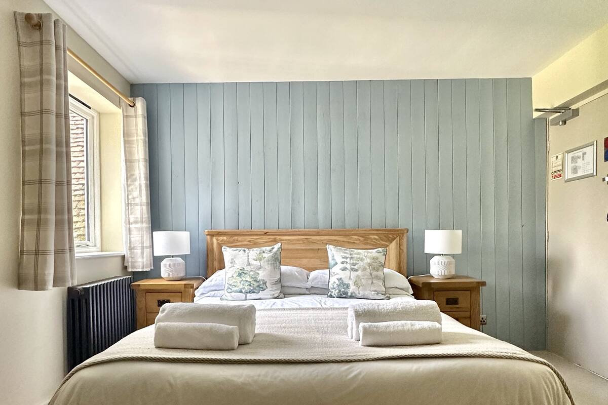 A neatly made bed with white linens and two pillows, flanked by bedside tables with lamps, in a room with a wooden headboard and light blue walls.
