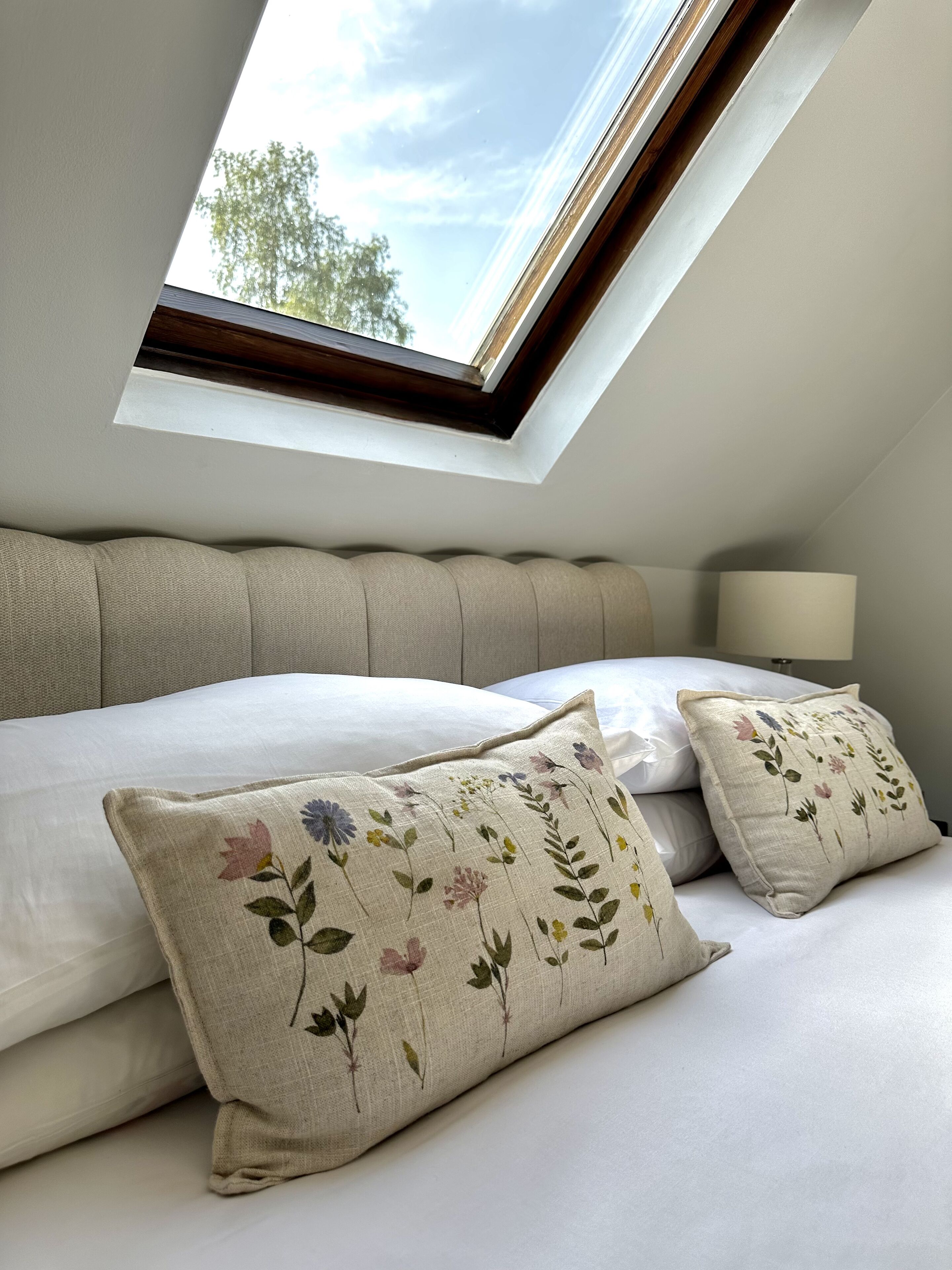 A bedroom with a skylight, a bed with floral pillows, and a nightstand with a lamp.