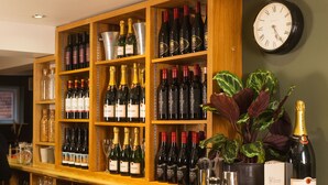 A bar area with shelves of wine bottles, a clock, and a potted plant. - The Manor at Abberley (Worcester)
