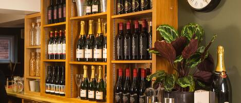 A bar area with shelves of wine bottles, a clock, and a potted plant.