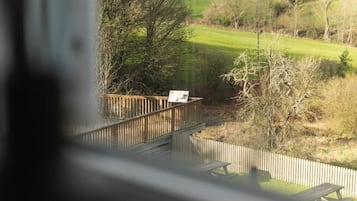 Een houten terras met een bankje, met uitzicht op een grasveld met bomen.