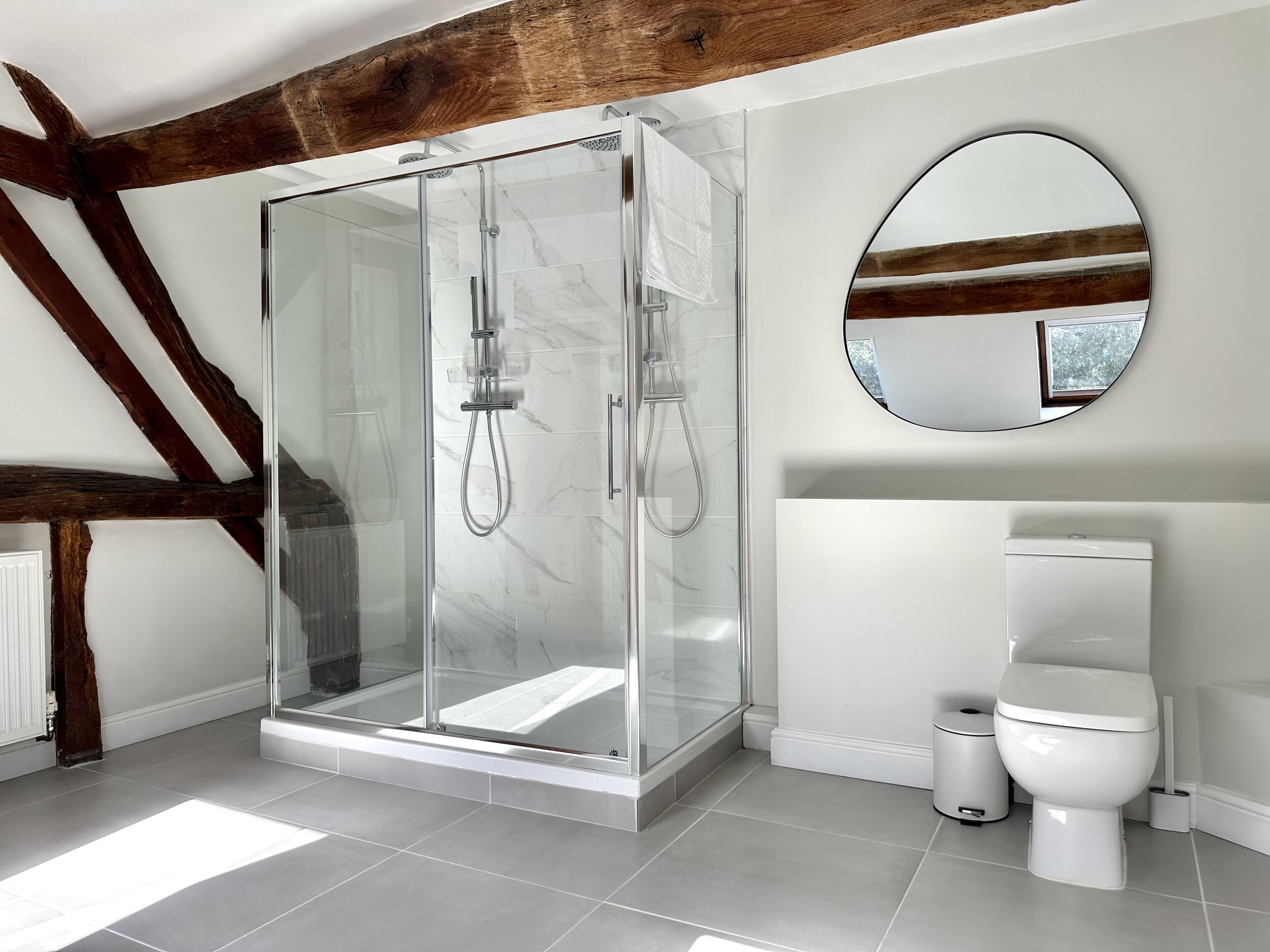 Un baño moderno con ducha de vidrio, inodoro blanco y un espejo redondo.