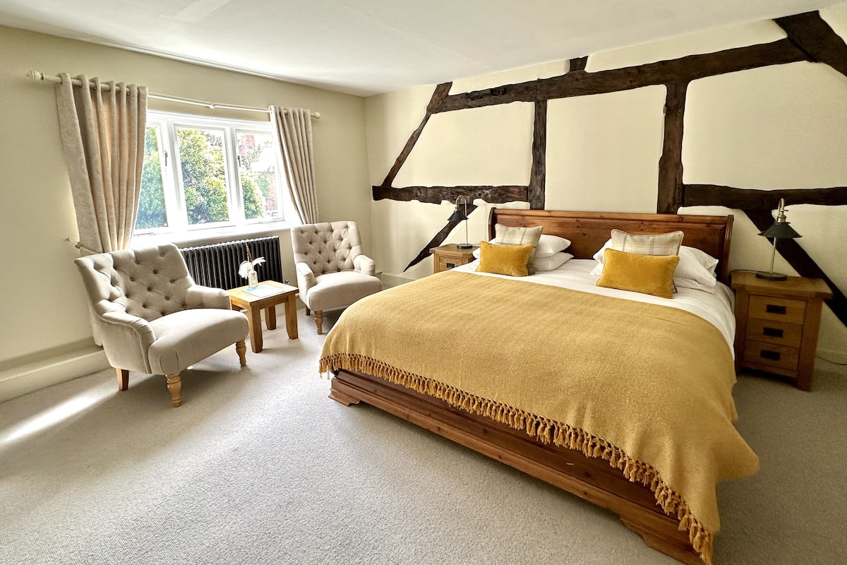 A bedroom with a large bed, two armchairs, a small table, and a window with curtains.