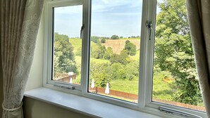 A window with a view of a green landscape, a wooden deck, and a white curtain. - The Manor at Abberley (Worcester)