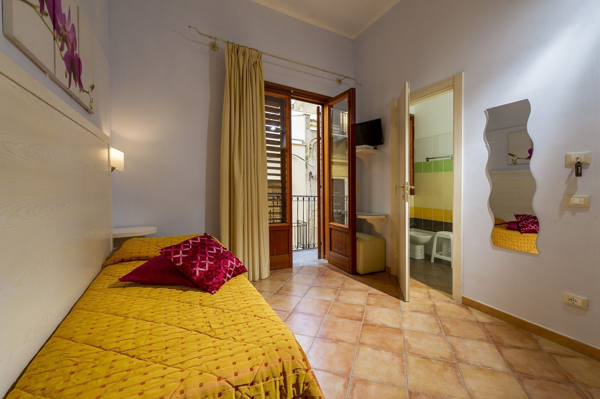 Una camera da letto con un letto, un bagno visibile attraverso una porta aperta e un televisore montato a parete.