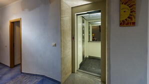 A hallway with a door leading to an elevator, a painting on the wall, and a carpeted floor. - Badia Rooms & Breakfast (Castellammare del Golfo)