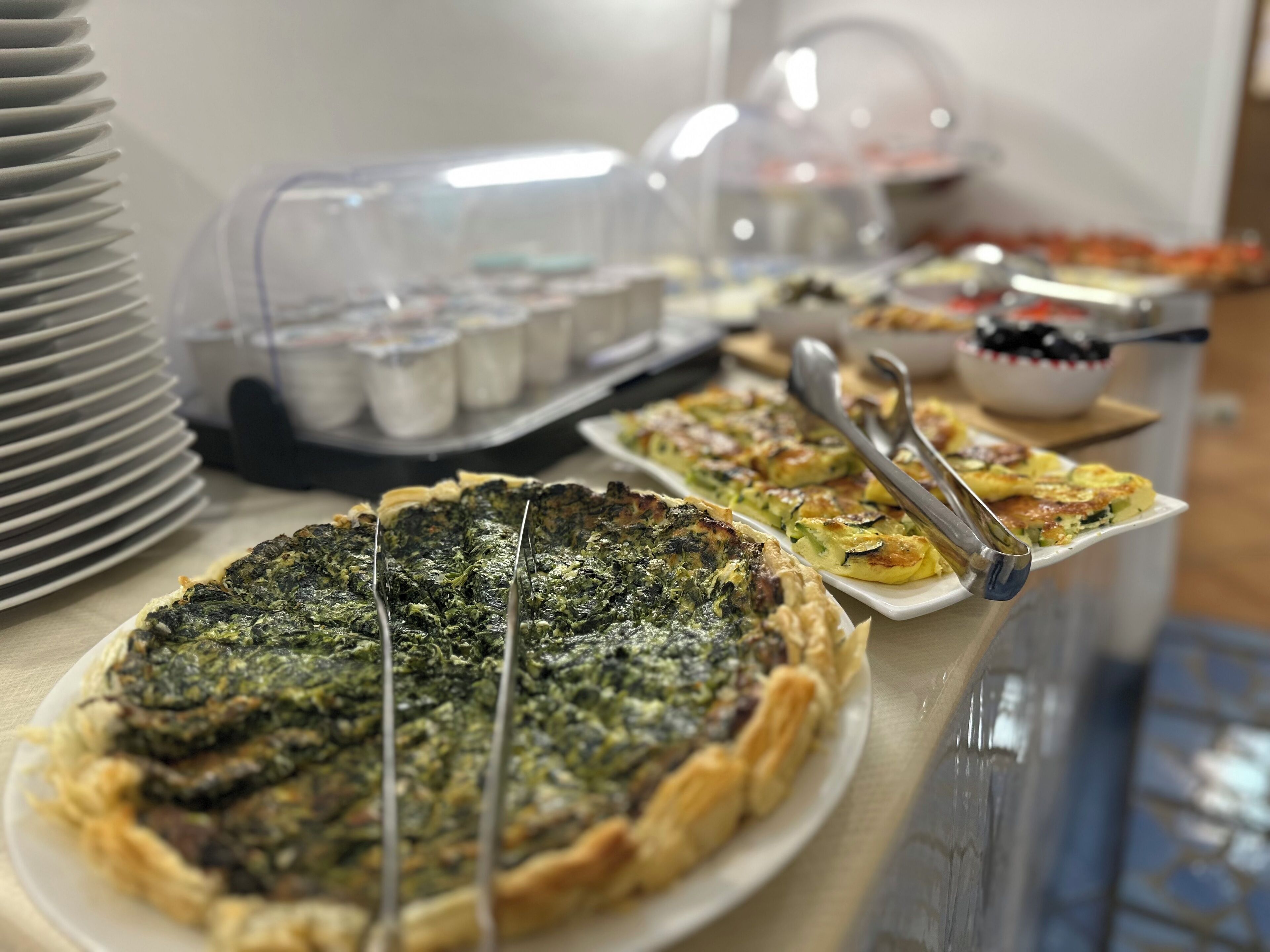 A buffet table with various dishes, including a quiche and a pie, and a bowl of fruit.