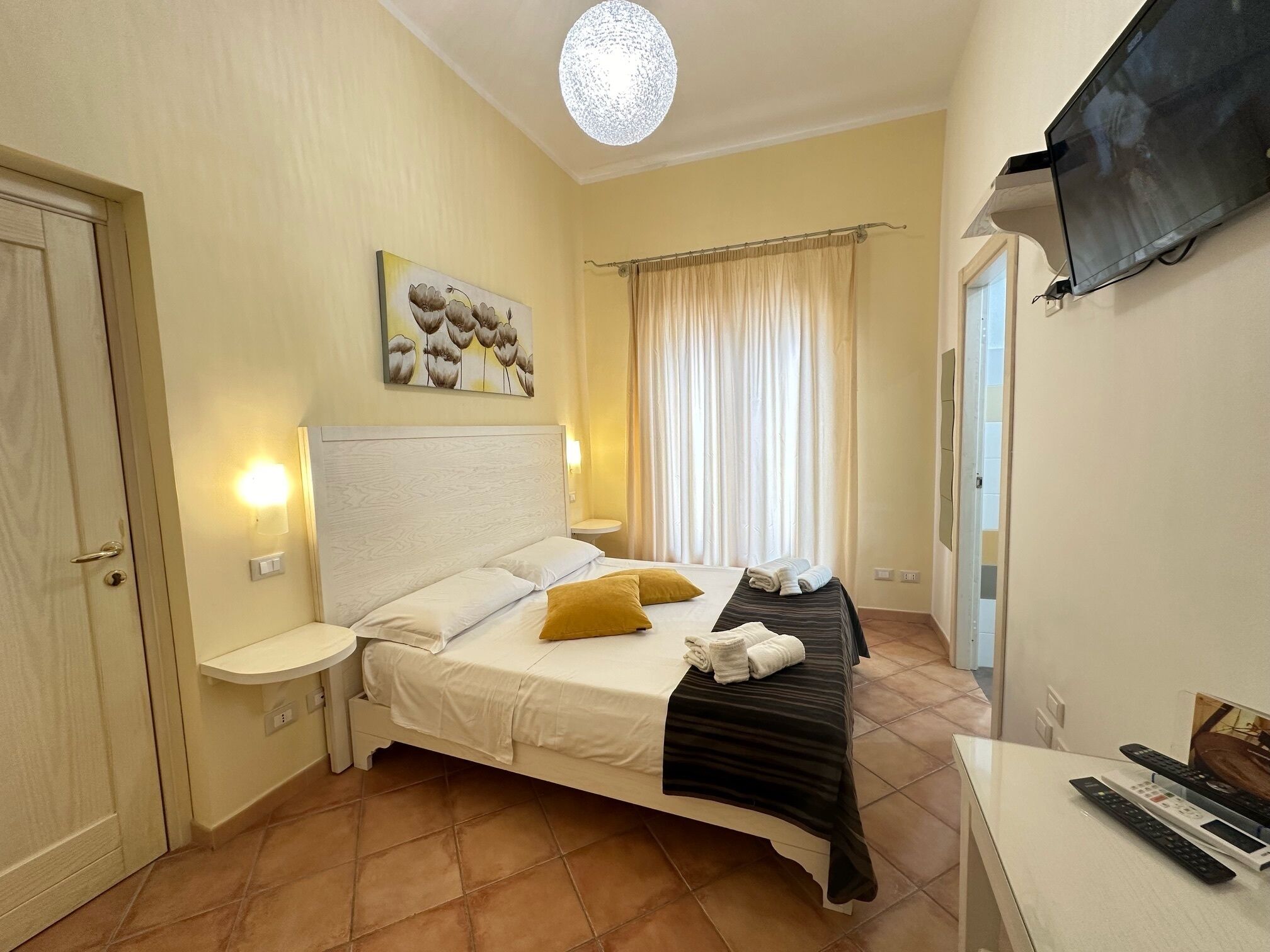 A hotel room with a bed, bedside tables, a flat-screen TV, and a painting on the wall.