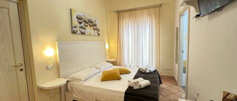 A hotel room with a bed, bedside tables, a flat-screen TV, and a painting on the wall.