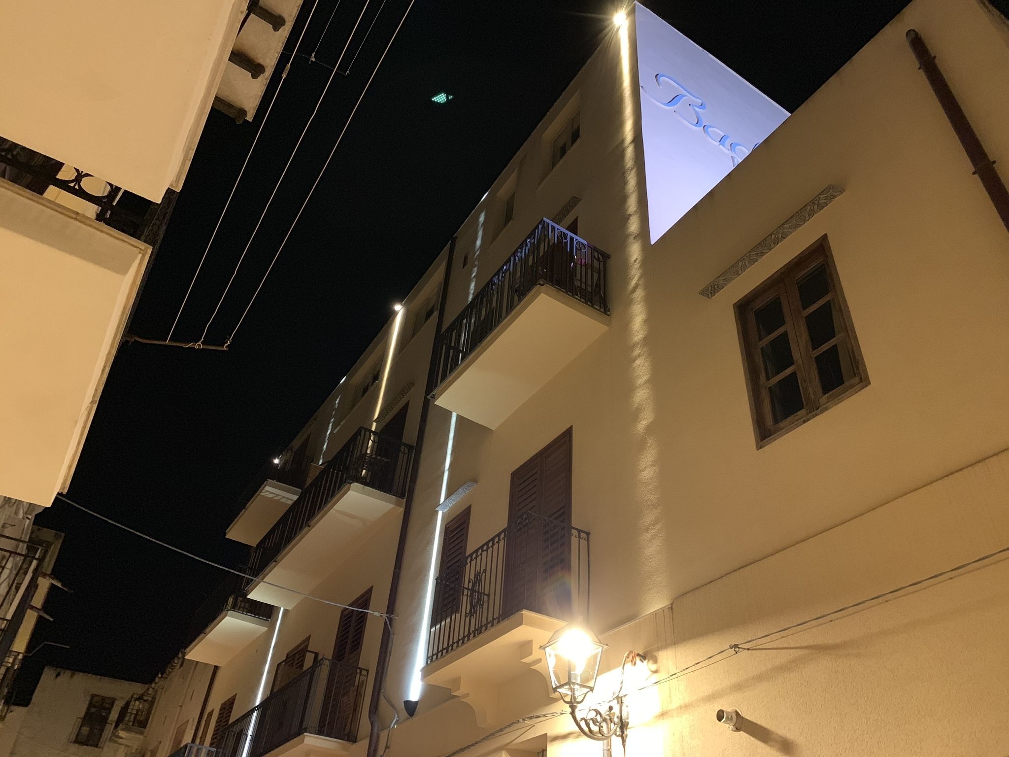 A narrow street with buildings featuring balconies and a lit sign.