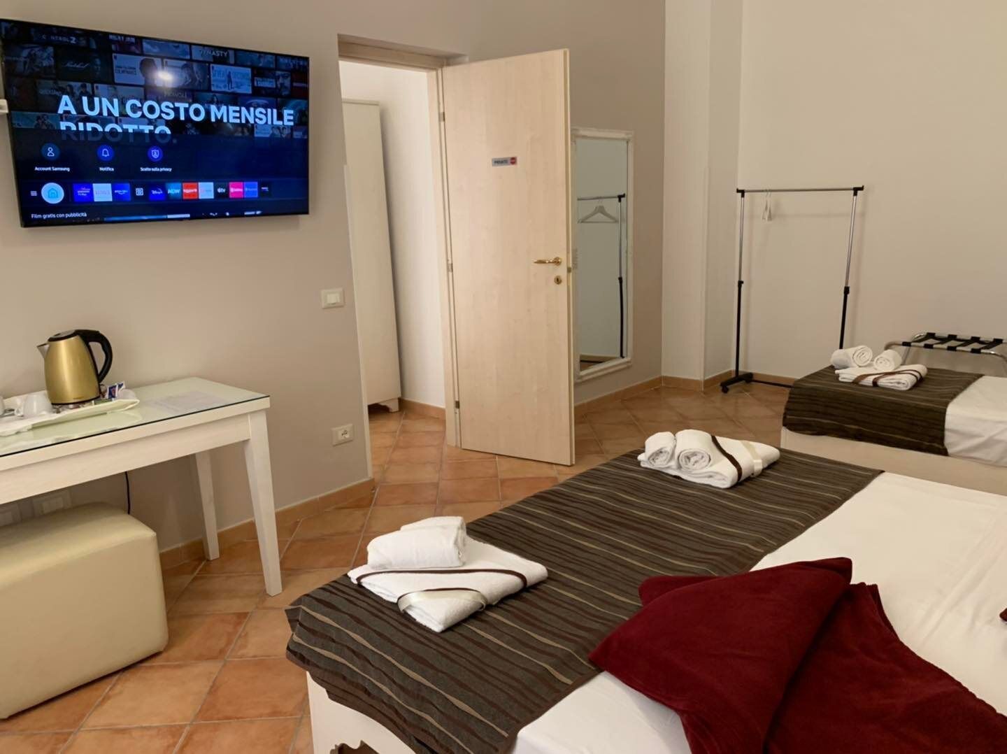 A hotel room with a bed, a desk, a television displaying a movie, and a bathroom visible through an open door.