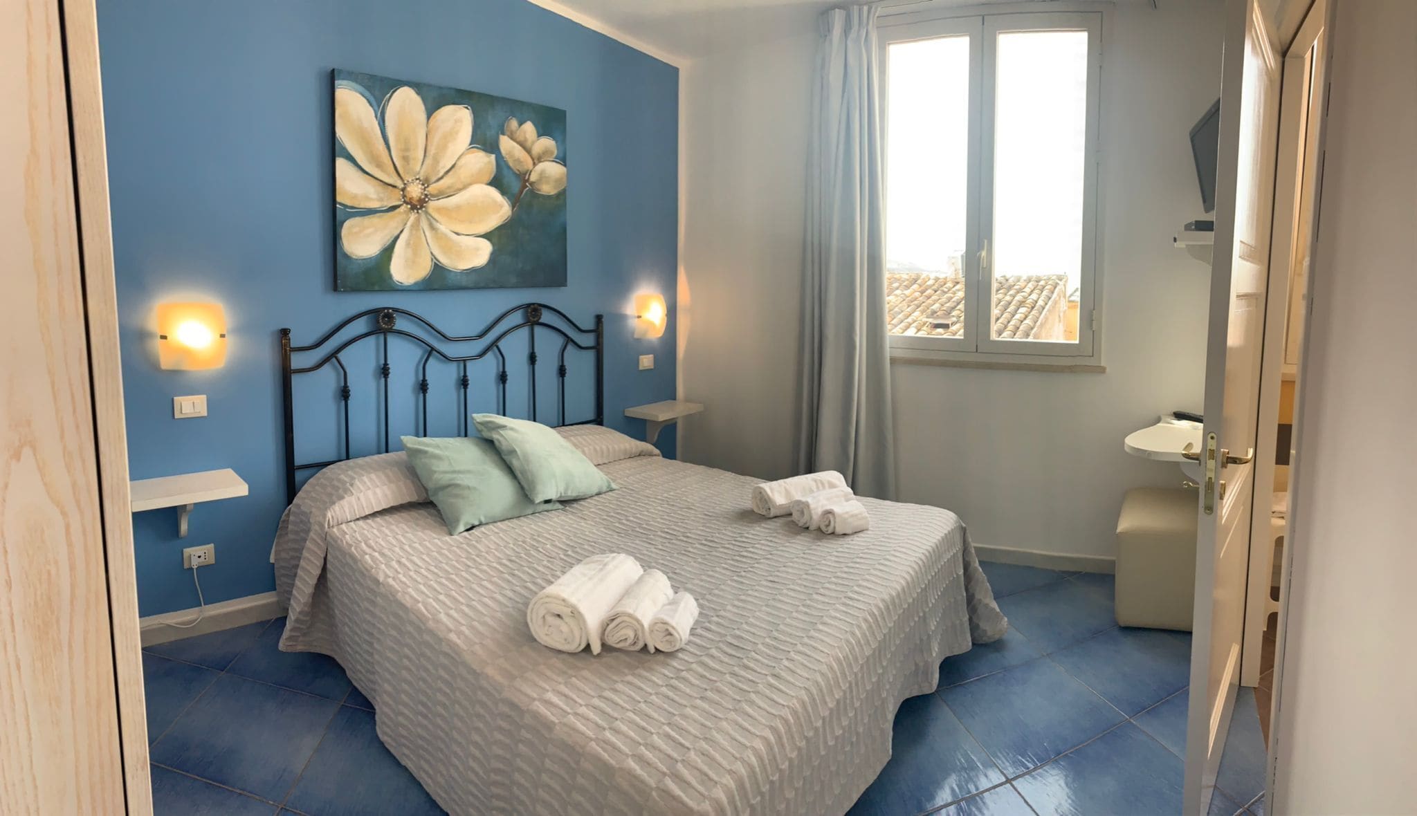 A bedroom with a bed, pillows, a painting, and a window.