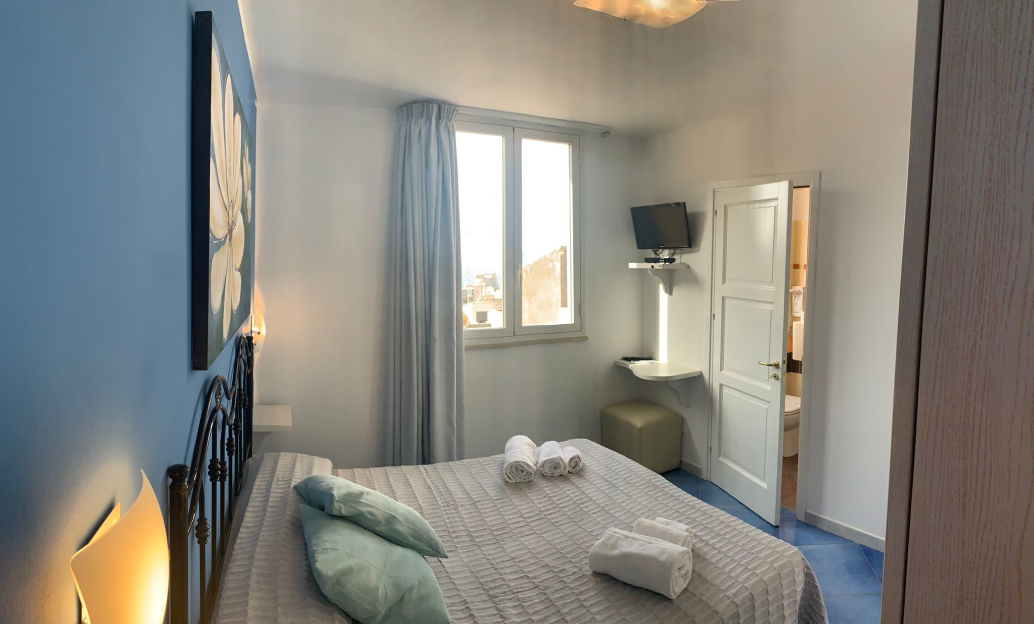 A bedroom with a bed, pillows, a TV, a window, and a bathroom door.