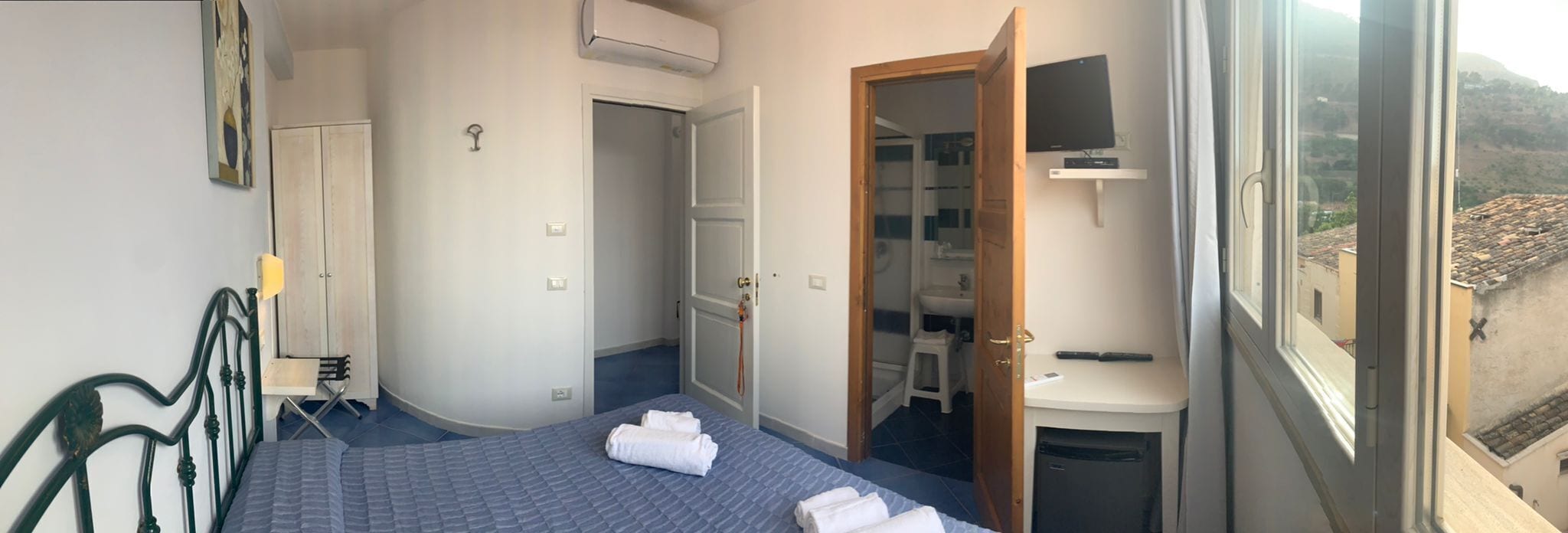 Quarto com cama, escrivaninha, cadeira, guarda-roupa e banheiro visível por uma porta aberta.