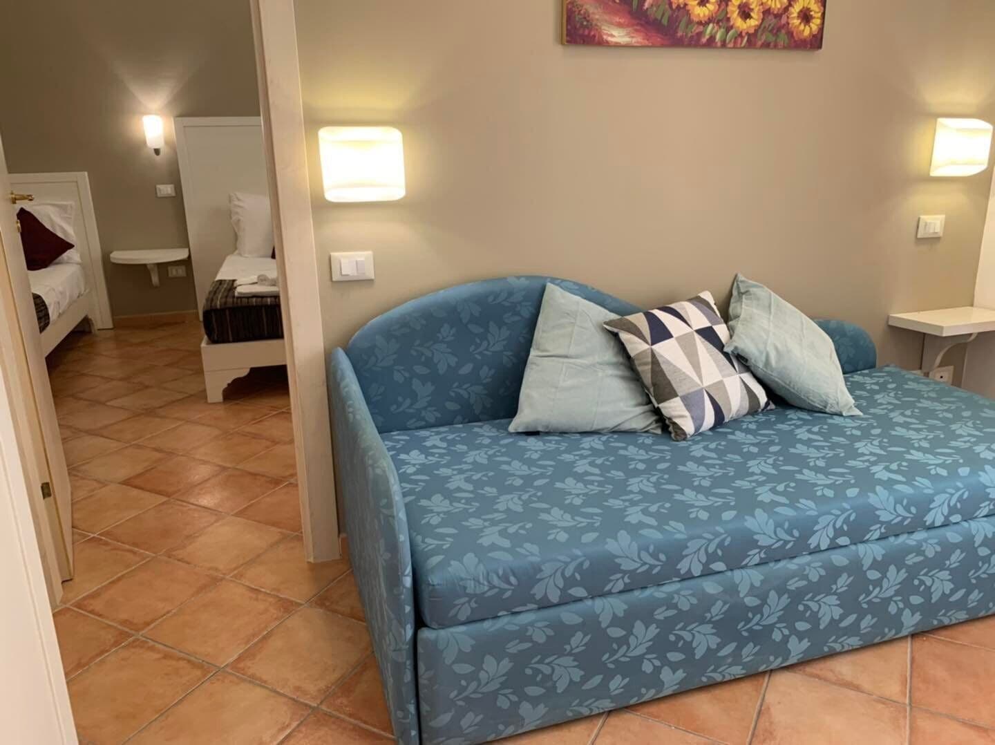 A bedroom with a blue floral sofa, a bed with a white headboard, and two bedside tables with lamps.