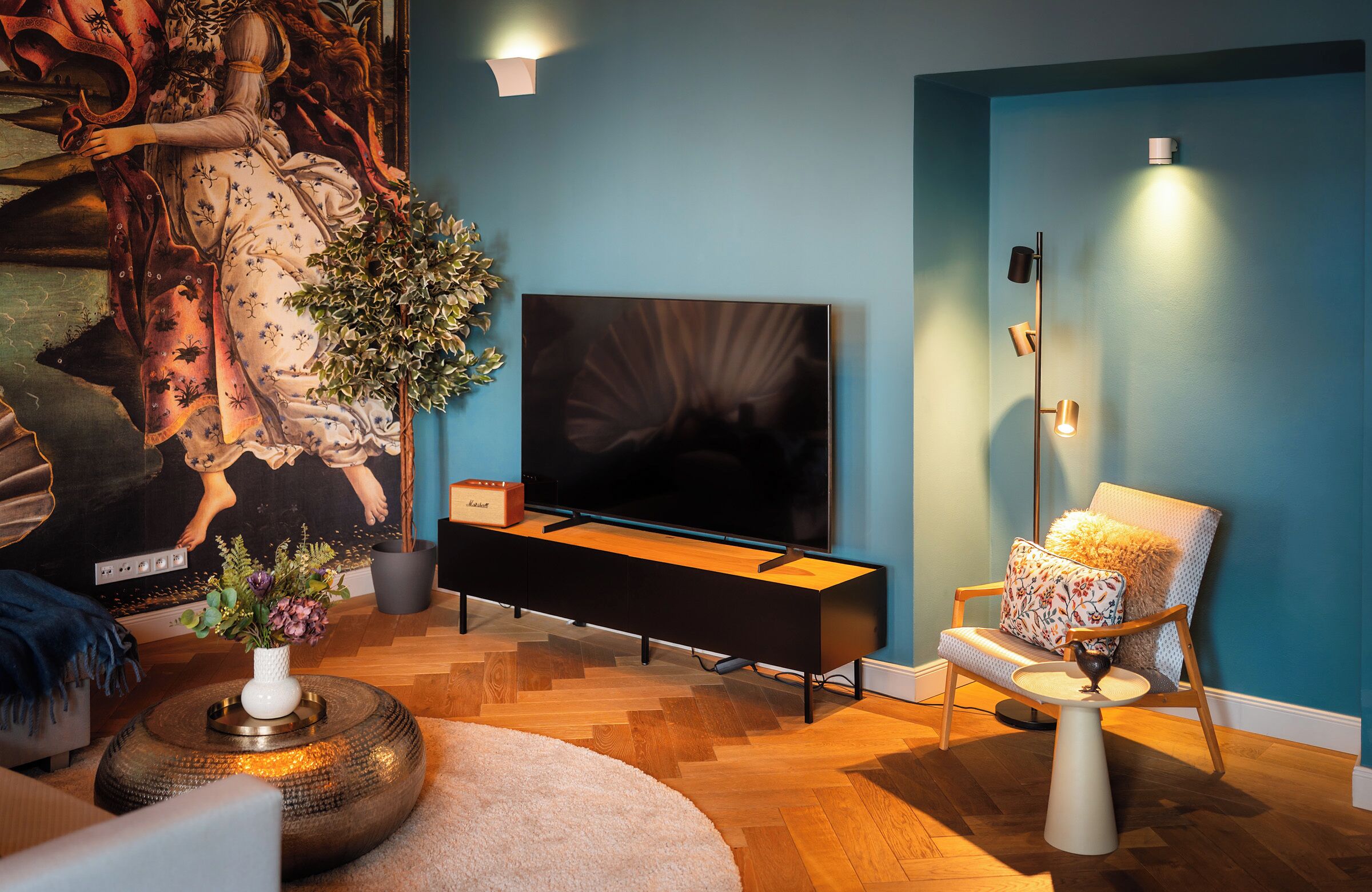 A modern living room with a large flat-screen TV, a decorative wall piece, a plant, and a stylish chair.