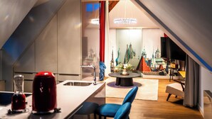 A modern kitchen with a central island, a dining area with a round table, and a view of a cityscape through a large window. - Old Royal Post Boutique Hotel & Premium Suites (Prague)