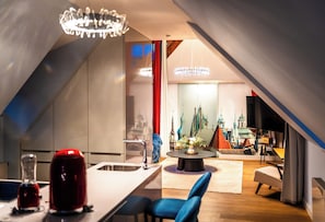A modern kitchen with a central island, a dining area with a round table, and a view of a cityscape through a large window. - Old Royal Post Boutique Hotel & Premium Suites (Prague)
