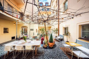 Ein Innenhof mit Sitzgelegenheiten im Freien, Blumentöpfen und Blick auf die umliegenden Gebäude.