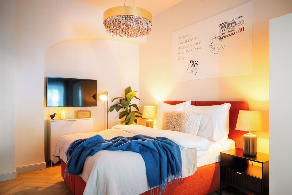 A modern bedroom with a large bed, bedside lamps, a television, and a chandelier.