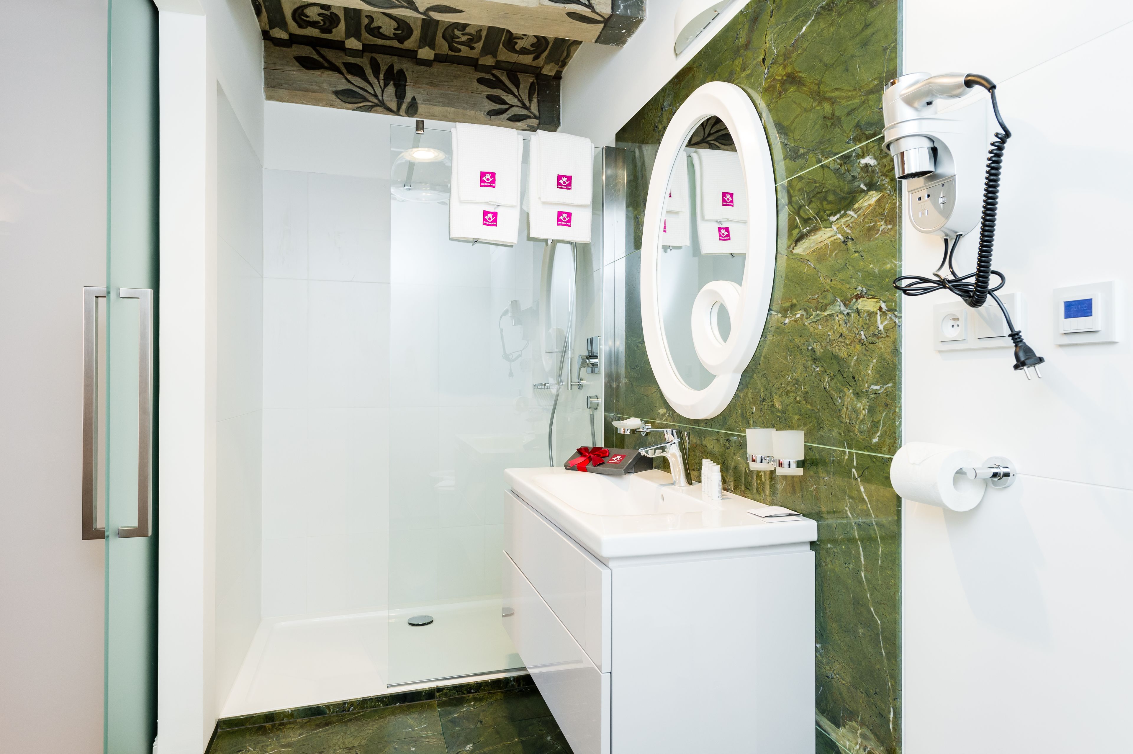 A modern bathroom with a glass-enclosed shower, a white sink with a marble countertop, and a hairdryer mounted on the wall.