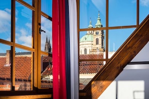 A room with a large window overlooking a historic building with a green dome and spires. - Old Royal Post Boutique Hotel & Premium Suites (Prague)