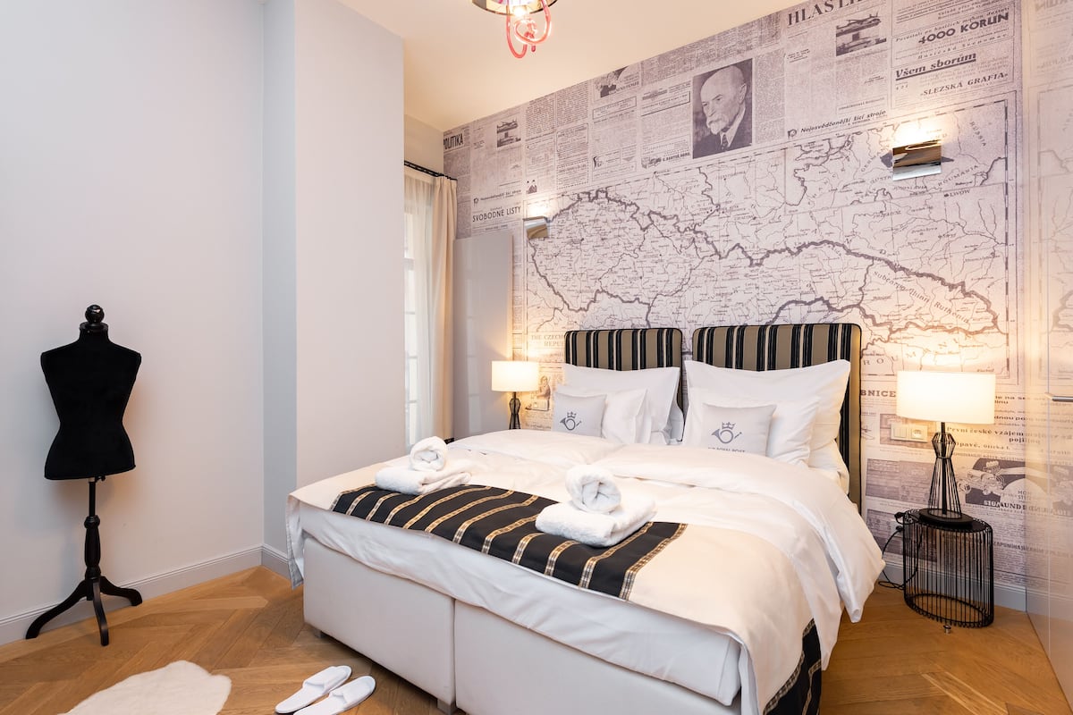 A neatly made bed with striped bedding, a mannequin, and a map-themed wall.