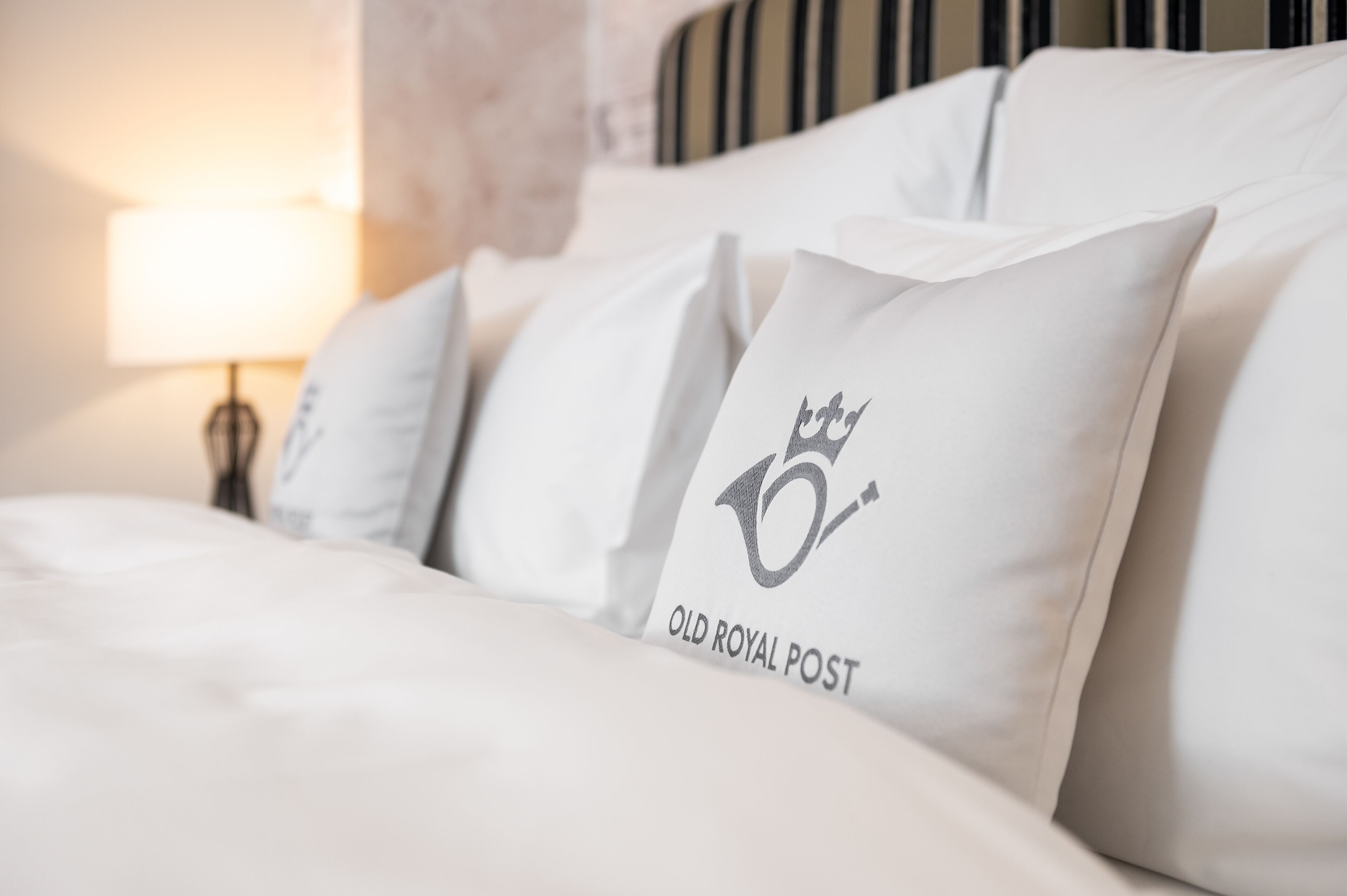 A bed with white bedding and pillows, one with a logo and text.
