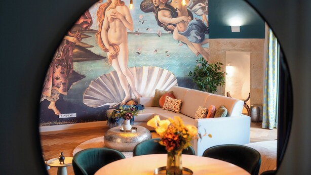 A modern living room with a large mural, a sofa, a coffee table, and a vase of flowers. - Old Royal Post Boutique Hotel & Premium Suites (Prague)
