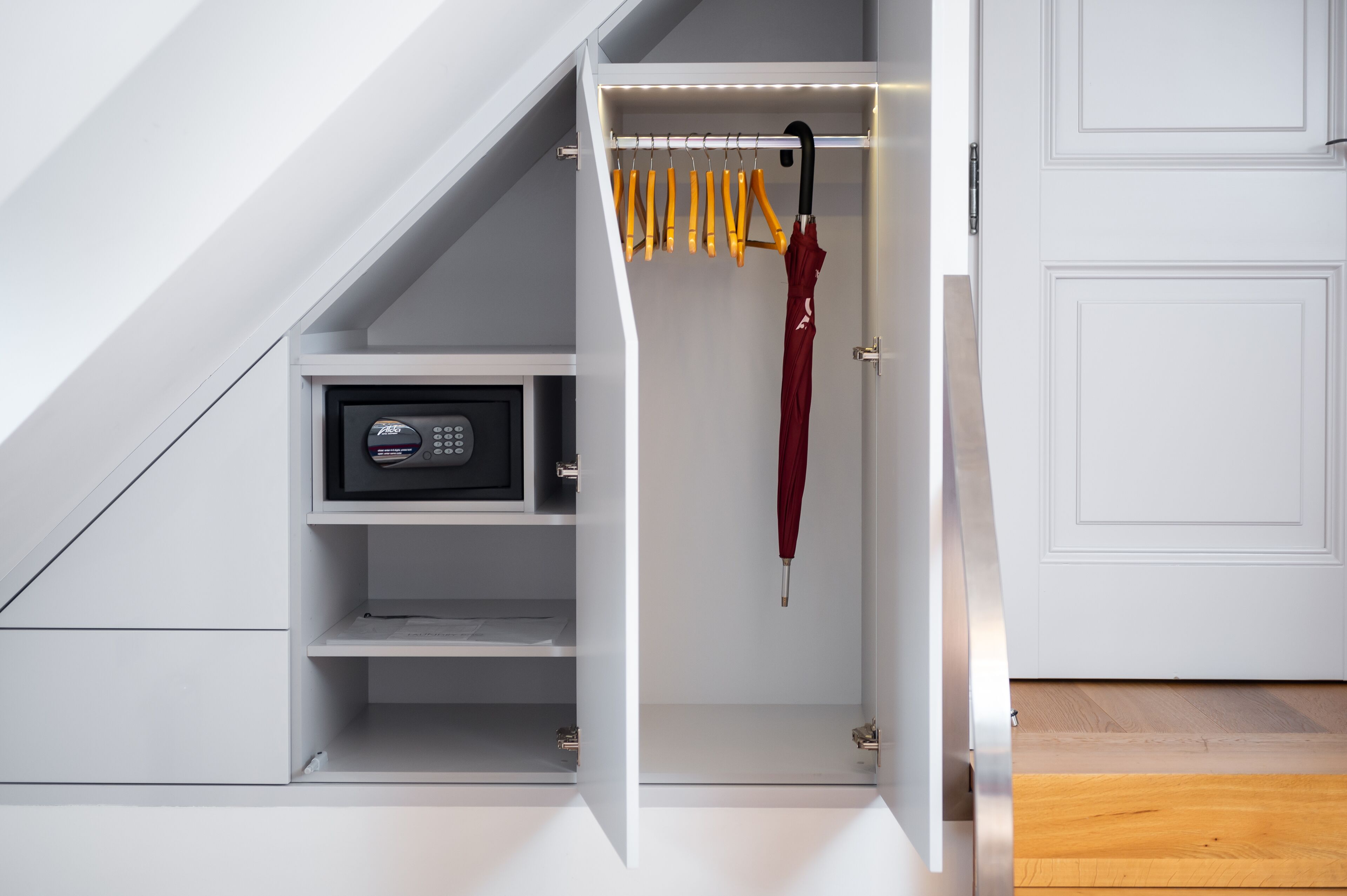 A modern closet with a built-in safe, a hanging rack with yellow handles, and a red umbrella.