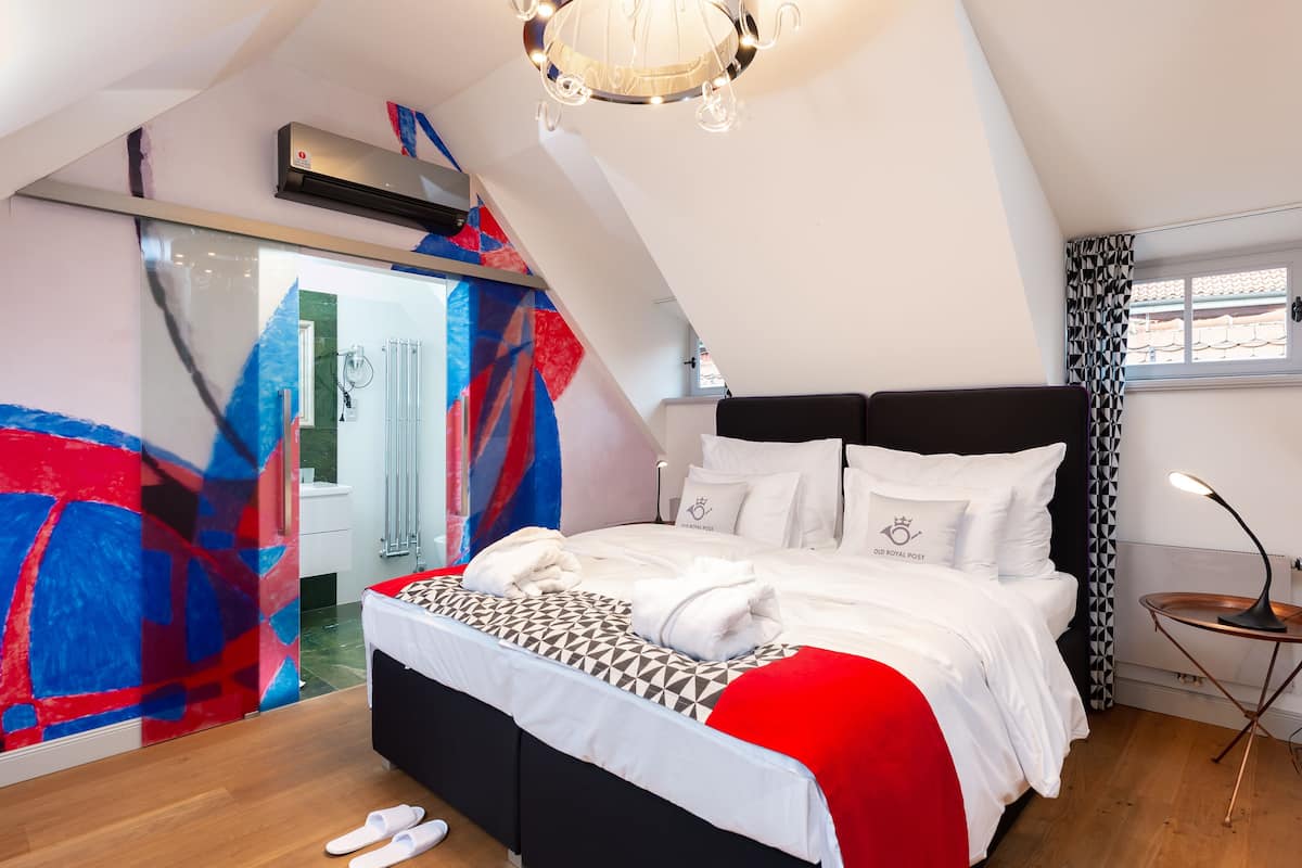 A modern bedroom with a black headboard, white bedding, and a red accent.