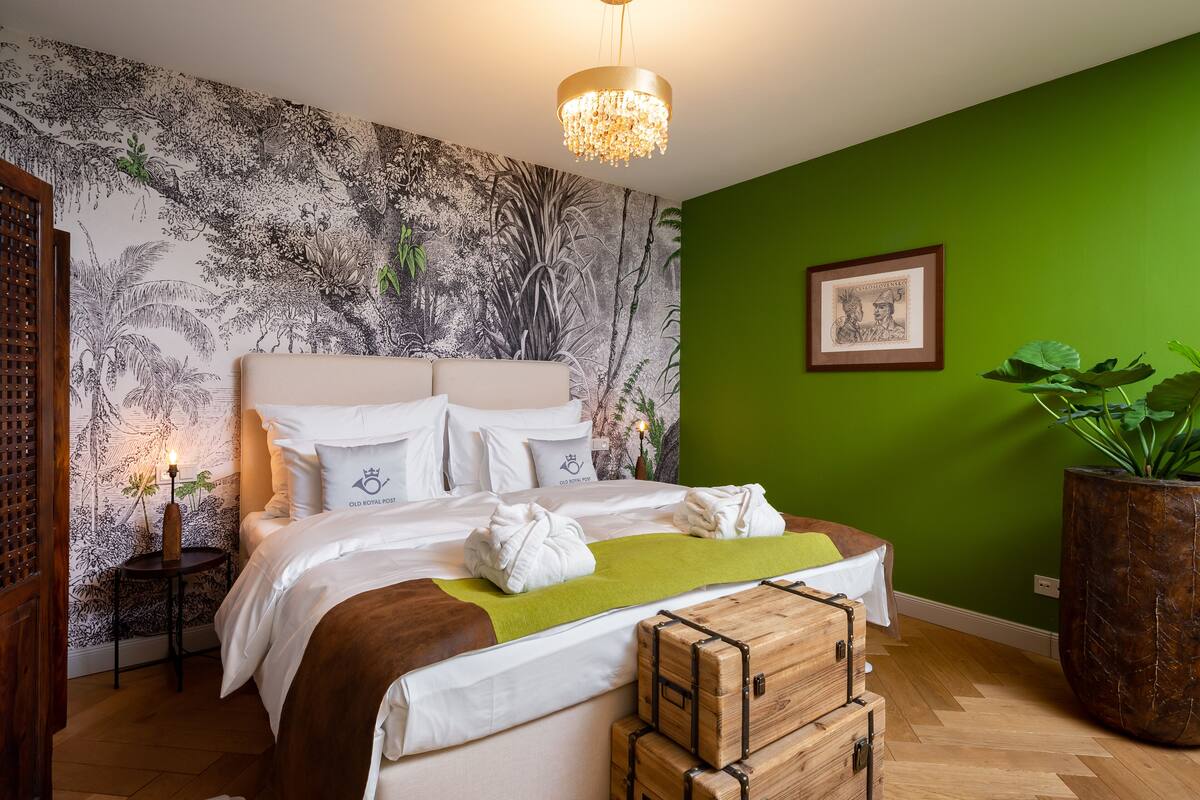 A neatly made bed with white linens, a green throw blanket, and a wooden trunk.