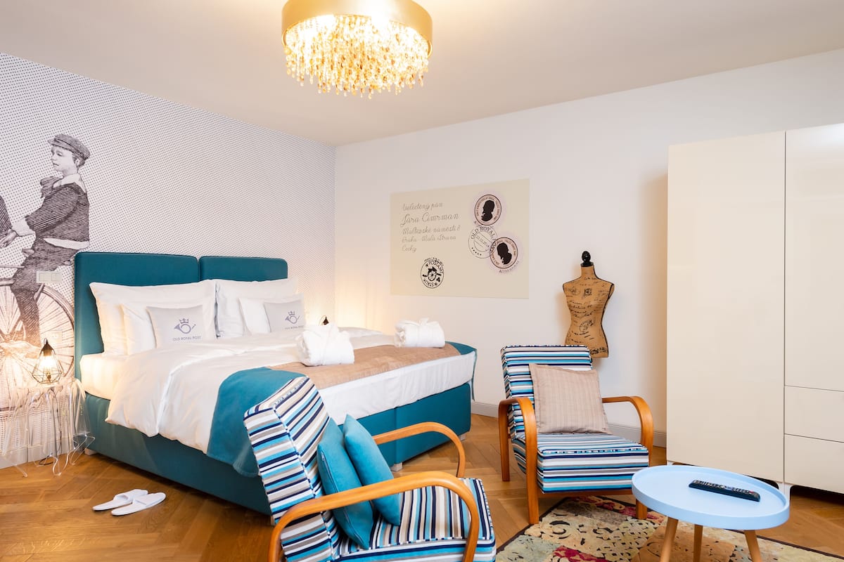 A modern bedroom with a large bed, a wooden chair, a small table, and a chandelier.