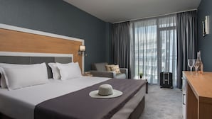A hotel room with a large bed, a desk, a chair, and a suitcase. - TM Deluxe Hotel (Sunny Beach)
