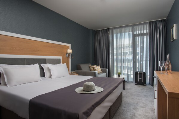 A hotel room with a large bed, a desk, a chair, and a suitcase. - TM Deluxe Hotel (Sunny Beach)
