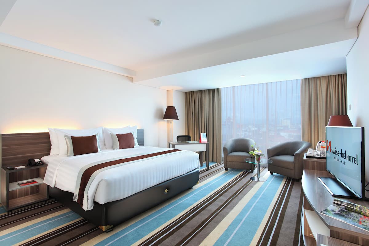 Una habitación de hotel moderna con una cama grande, un escritorio, un televisor y vistas a la ciudad.